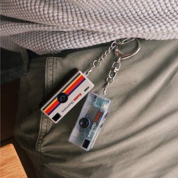 Two camera-themed keychains hang from a chain attached to a belt loop, showcasing retro Kodak designs