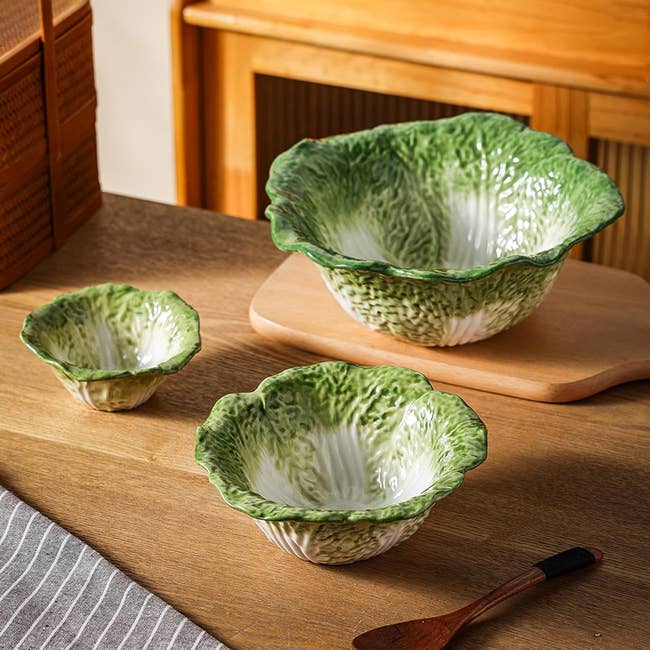 Three ceramic bowls resembling lettuce beryllium   connected  a woody  table, showcasing a originative  kitchenware design