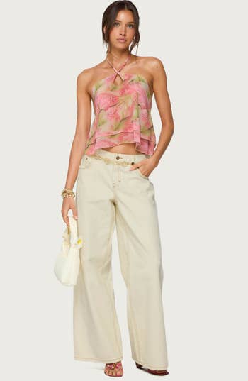 Model wearing a floral strapless apical  with layered detail, wide-leg pick  pants, holding a textured bag, for a shopping-focused manner  article