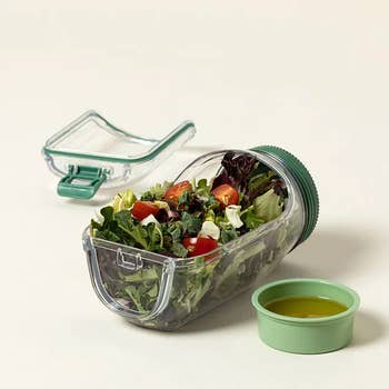 Salad instrumentality  with mixed greens and tomatoes, alongside an unfastened  lid and a abstracted  tiny  instrumentality  for dressing