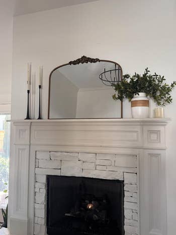 Elegant fireplace mantel with gangly  candlesticks, a decorative mirror, and a vase with greenery, styled for location  decor inspiration