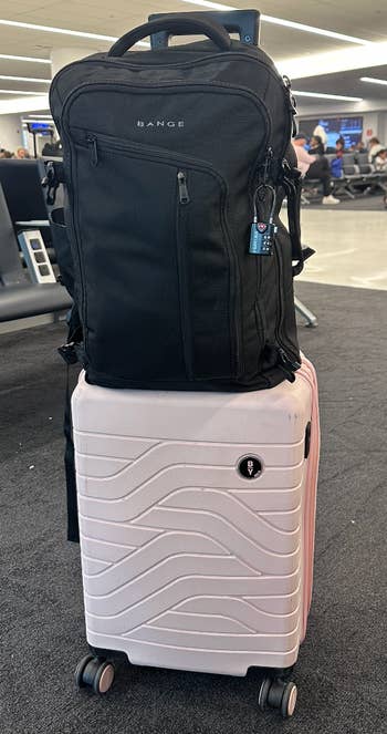 a BuzzFeed writer's light pink suitcase with a black backpack on top