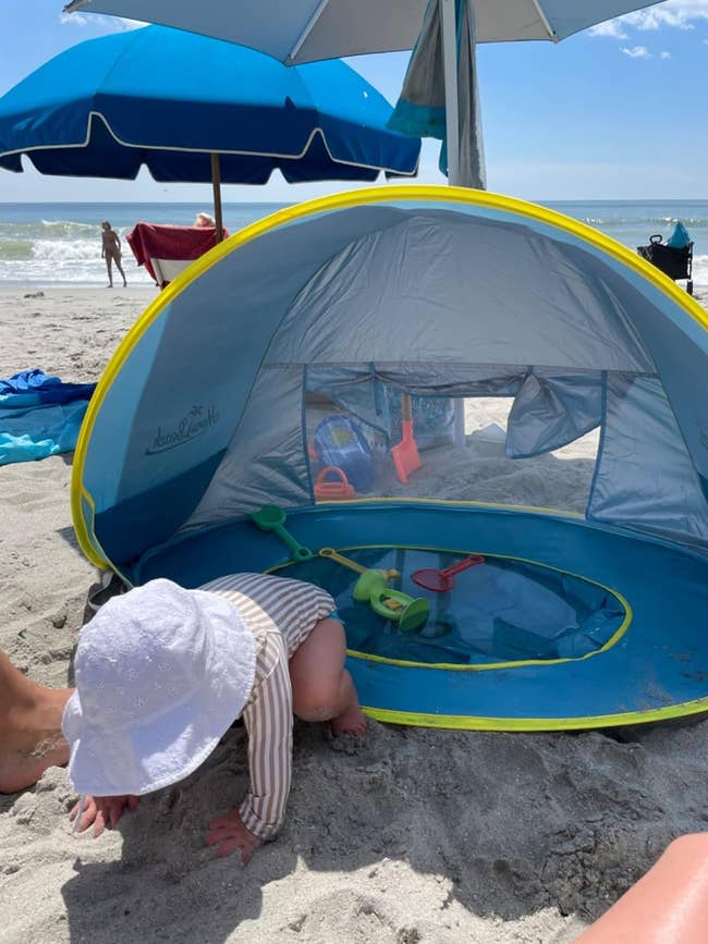 A reviewer's baby is playing on the beach under a small tent with toys inside
