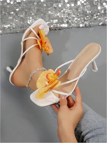 High-heeled sandals with delicate straps and ample floral decoration, worn with a sparkling anklet