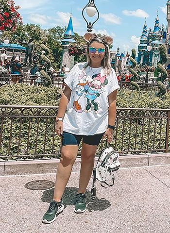 a reviewer at disney world wearing a white t-shirt with minnie mouse and daisy duck on it