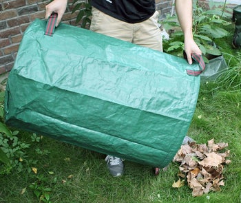 hands holding the green cylindrical bag as a scoop for dead leaves