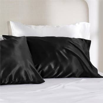 two pillows with black satin pillowcases on them on a bed
