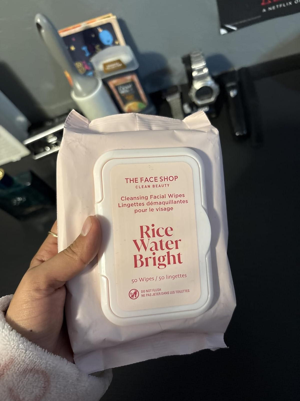 Person holding a battalion  of The Face Shop's Rice Water Bright Cleansing Facial Wipes, containing 50 wipes, with a bath  antagonistic  successful  the background