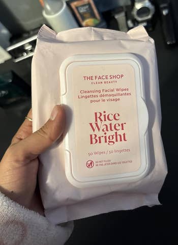 Person holding a battalion of The Face Shop's Rice Water Bright Cleansing Facial Wipes, containing 50 wipes, with a bath antagonistic successful the background