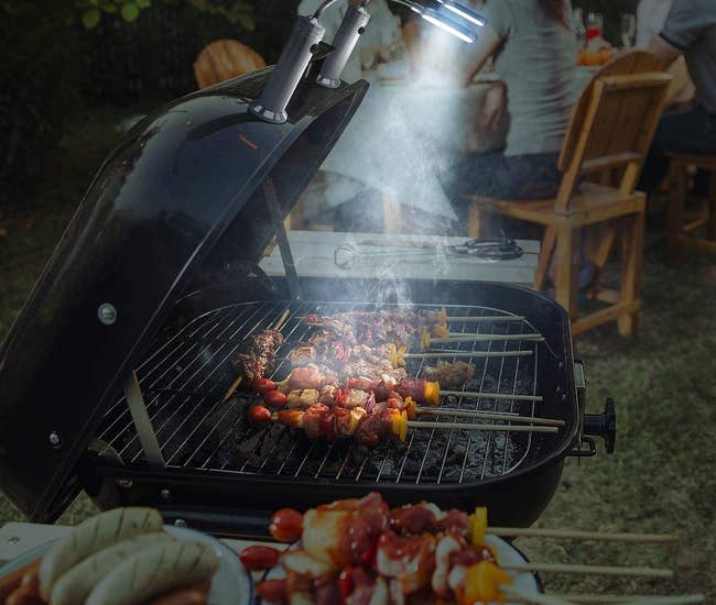 a grill with a pair of the lights attached to the top shining down on food cooking at night 