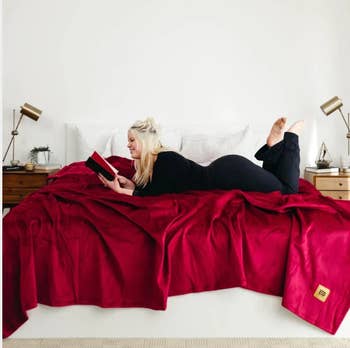 a bed with the blanket in red on top and a model laying across it