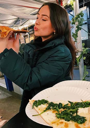 a reviewer wearing the coat in green, eating pizza