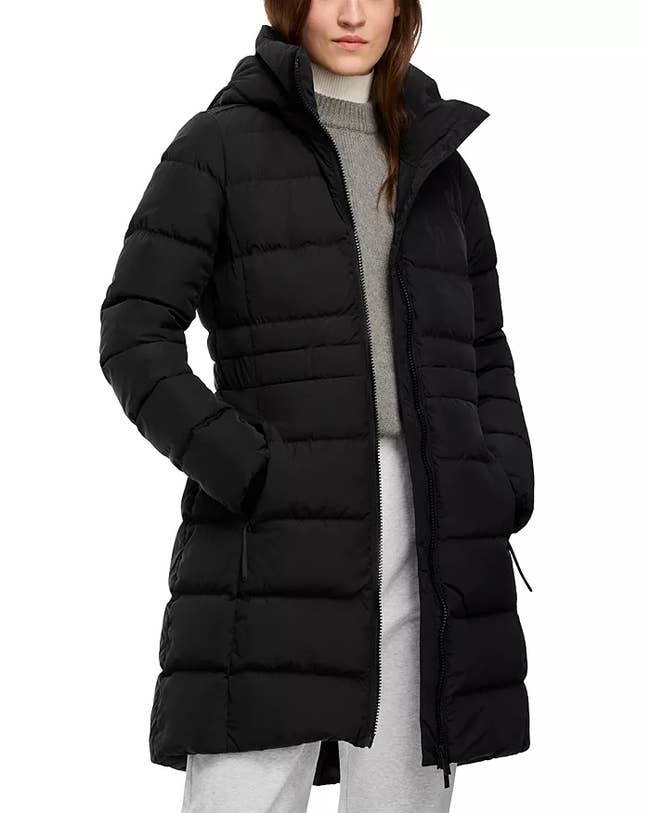 Person wearing a long, padded wintertime overgarment with a hood, paired with a turtleneck sweater and casual pants