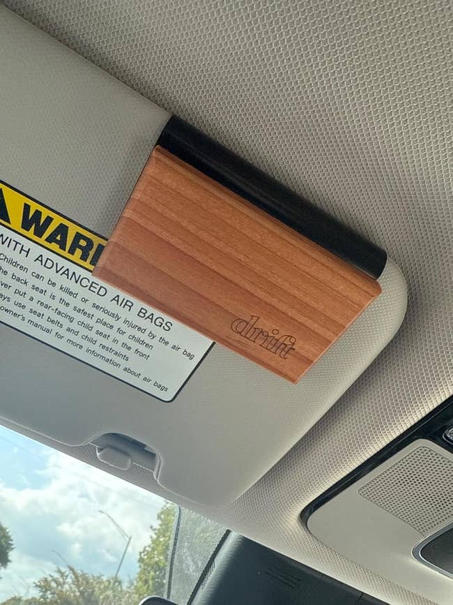 Penyegar udara kayu terpotong ke pelindung matahari mobil di sebelah label peringatan airbag. Penyegar dicap dengan