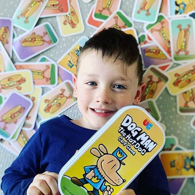 child model holding Dog Man game while laying on the cards