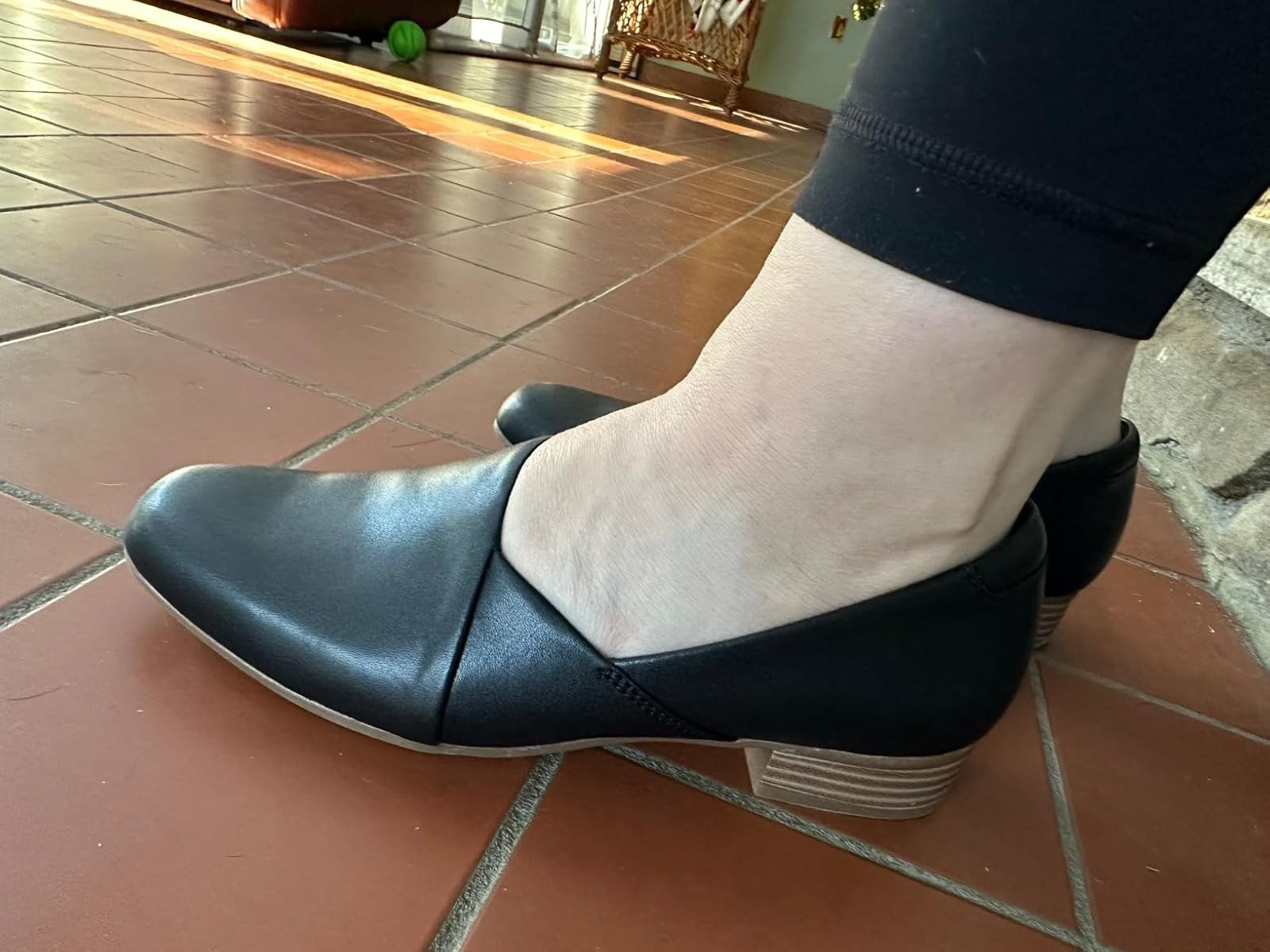 Person wearing sleek, slip-on achromatic  flats with a airy  woody  heel, lasting  connected  a tiled level  indoors
