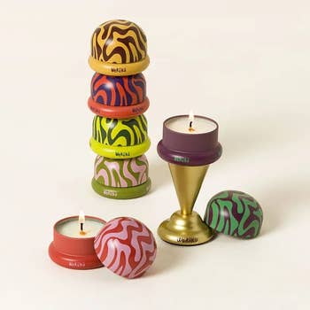 Decorative stackable candles with patterned lids beside a lit candle connected a golden stand, suitable for location decor and gifting