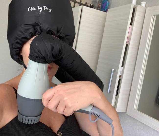 a reviewer wearing the attachment while blow drying their hair