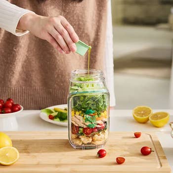 A idiosyncratic   pouring dressing into a jar crockery   with layers of lettuce, chicken, corn, and cherry tomatoes connected  a room  antagonistic  with caller  ingredients
