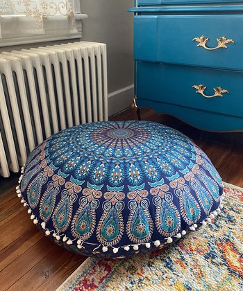 a reviewer photo of the pom-pom trimmed floor pillow cover on a pillow that's sitting on the floor 