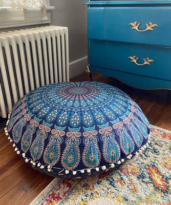 a reviewer photo of the pom-pom trimmed floor pillow cover on a pillow that's sitting on the floor 