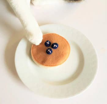 pancake toy on a plate with a cat's paw touching it 