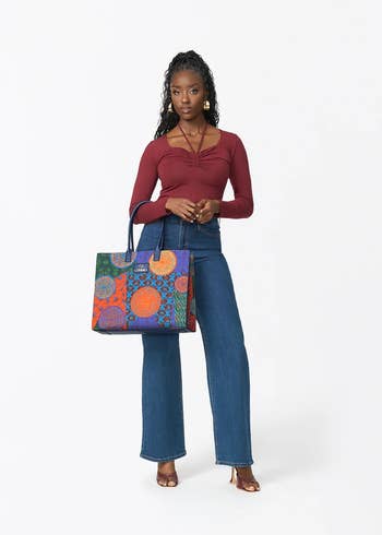 Person wearing a stylish apical and jeans, holding a large, patterned tote bag