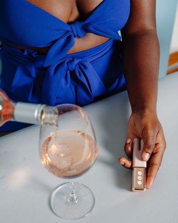 Model pouring glass of rosé and holding rose gold vibrator