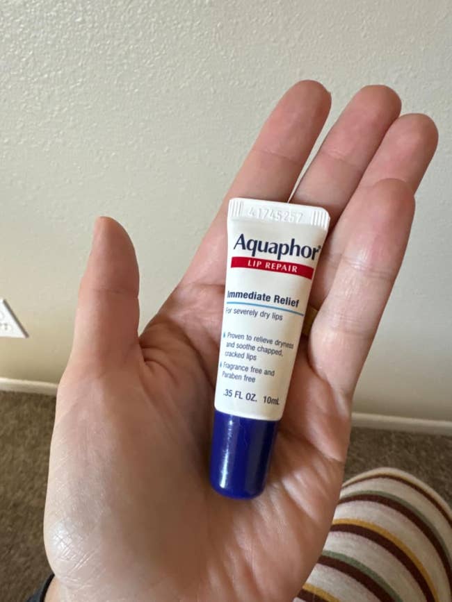 Hand holding a small tube of Aquaphor Lip Repair, labeled as immediate relief for severely dry lips