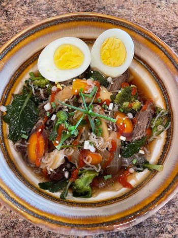 A vessel  of ramen with beef, vegetables, sliced boiled ovum  connected  top, garnished with herbs, served successful  a ceramic bowl