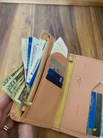 An open wallet with various credit cards, cash, and receipts displayed, held by a person with a ring on their finger
