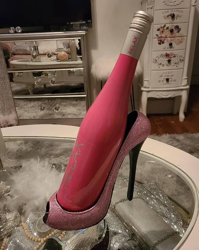 A glittery pink oversized high heel holding a wine bottle up 
