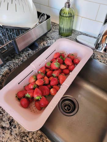 the pink strainer stretched over a sink draining strawberries