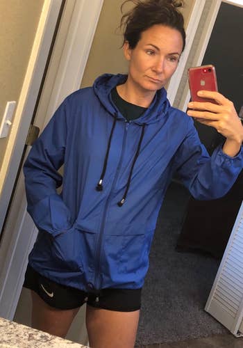 Person in a blue jacket and black shorts taking a selfie in a mirror