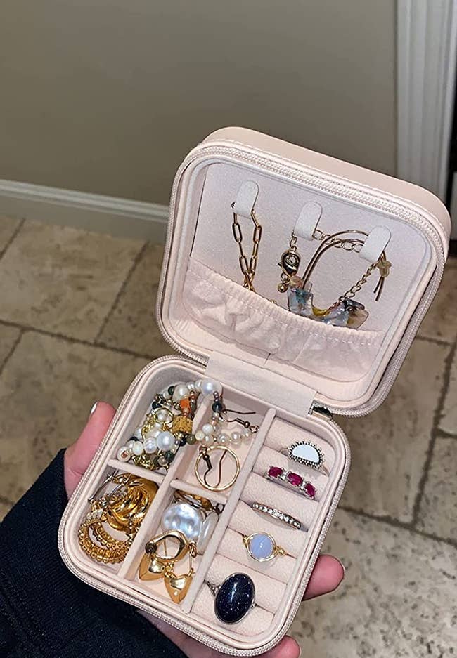 reviewer holding the small square jewelry box in beige, showing all the jewelry they fit in it