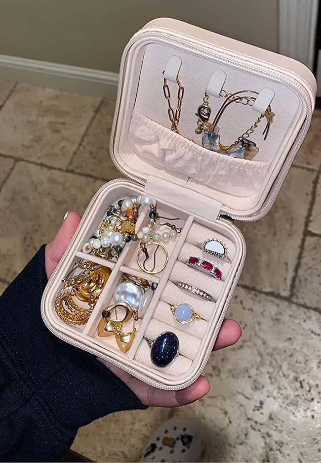reviewer holding the small square jewelry box in beige, showing all the jewelry they fit in it