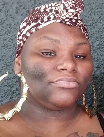 Person wearing large hoop earrings and a patterned headwrap, looking into the camera with a neutral expression