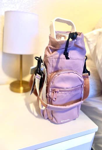 a lavender colored water bottle-shaped bag with a zippered front pocket and long handle 