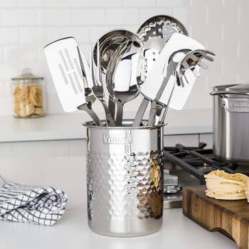 A variety of stainless steel kitchen utensils in a decorative holder on a kitchen counter