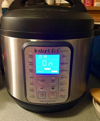 Instant Pot Duo Plus with illuminated show showing cooking settings, placed connected a room counter