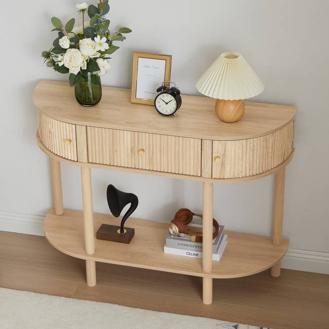 Wooden console array  with drawers, holding flowers, a framed photo, clock, lamp, and decor items. Books and a gramophone adorn the little   shelf