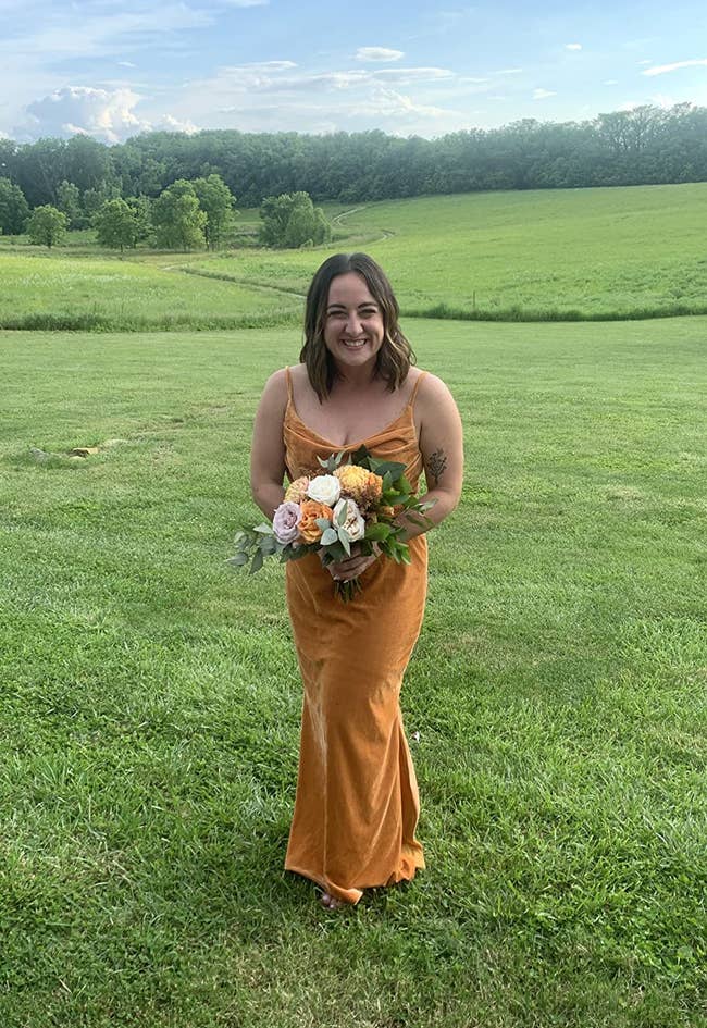 a reviewer wearing the mustard color dress and holding a bridesmaid bouquet 