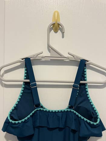 Ruffled swimsuit apical  with adjustable straps connected  a hanger against a plain background