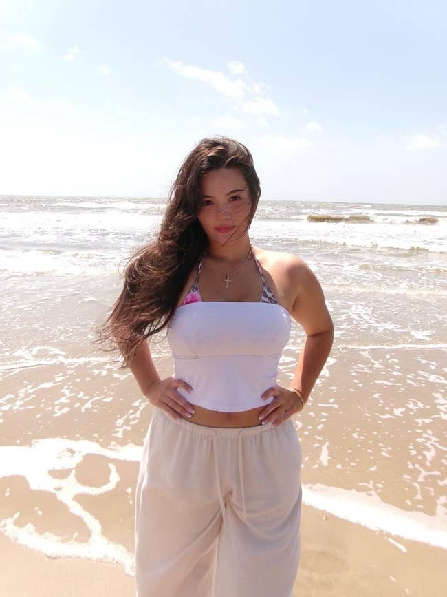 Person connected  a formation  wearing a halter apical  and escaped   pants, lasting  by the shoreline with windswept hair