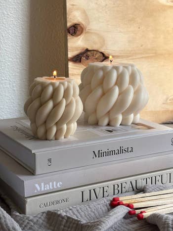 Two decorative, sculpted candles lit connected  stacked manner  and plan  books