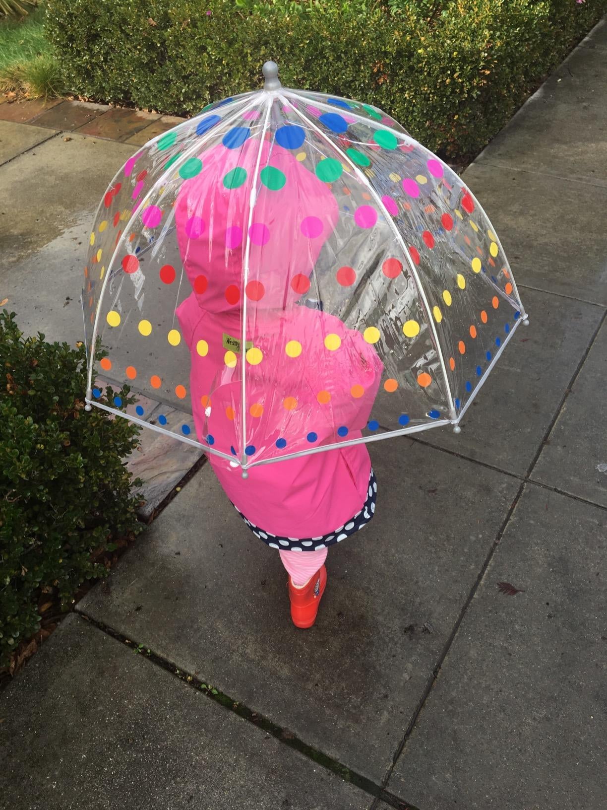 Reviewer's child walking in the rain holding the clear umbrella with colorful dots