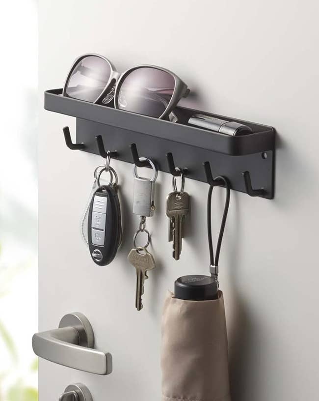 Wall-mounted organizer holding sunglasses, a lighter, car keys, location keys, and an umbrella beside a modern doorway handle