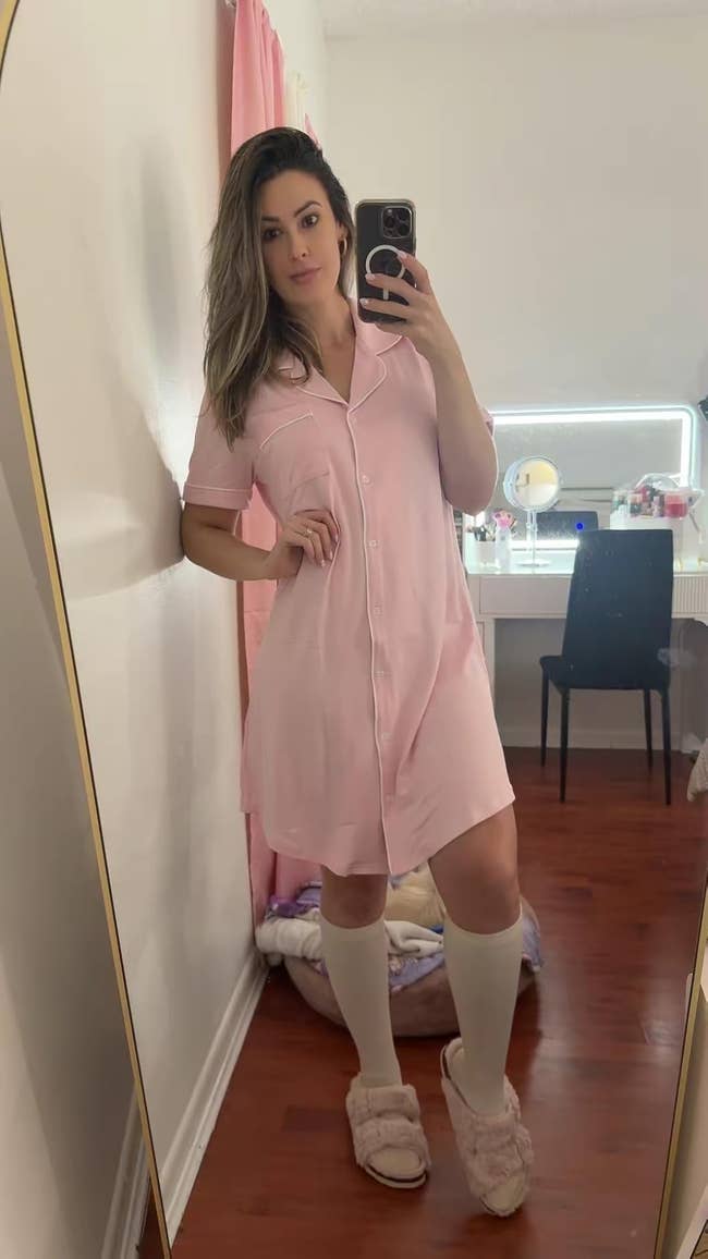 Person successful a button-down nightshirt and slippers, posing successful beforehand of a vanity reflector successful a cozy chamber setting