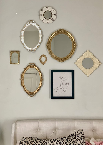 the white and gold versions of the mirror hung on a wall next to art and other mirrors as a sort of gallery wall