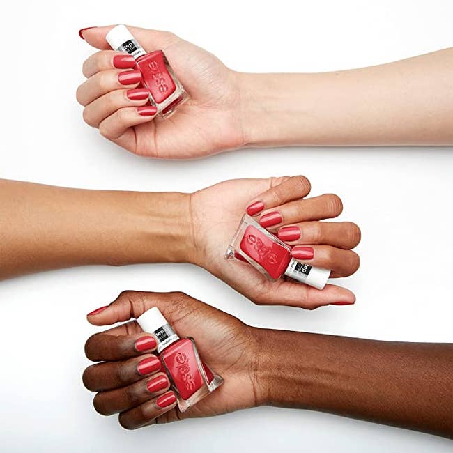 three hands holding a bottle of red nail polish, also painted on their fingers